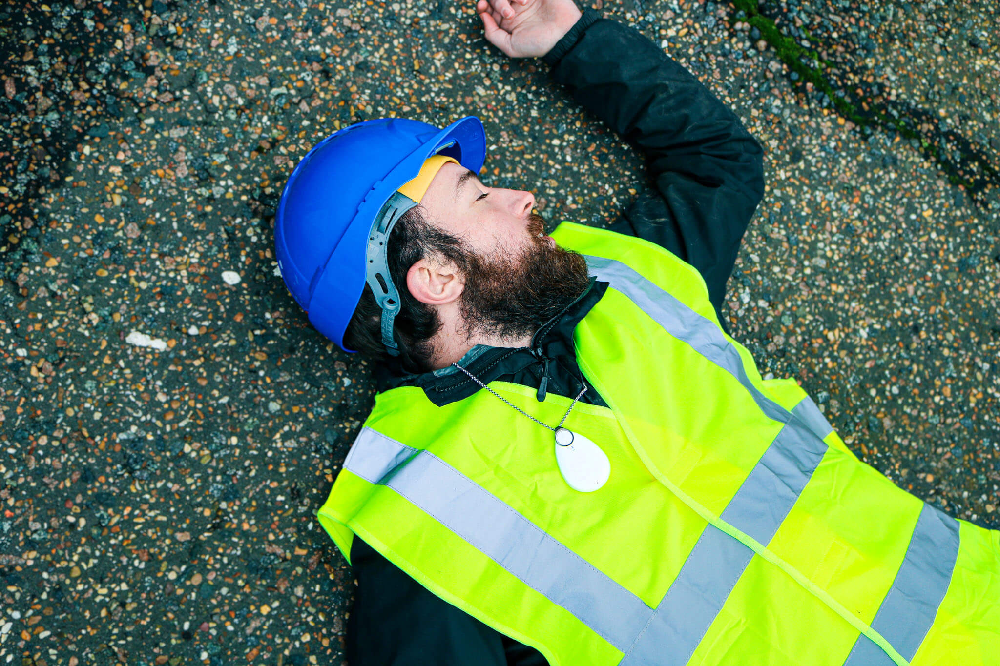 A Lone Worker wearing hi-vis and safety helmet lies on the ground