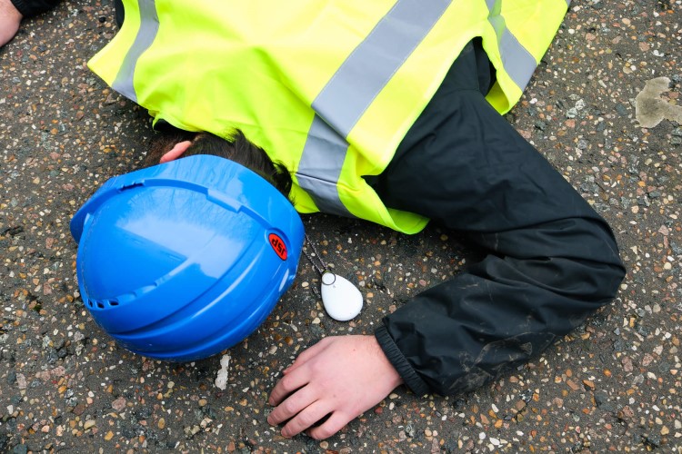A lone worker in high vis jacket and hard hat lies injured on the ground